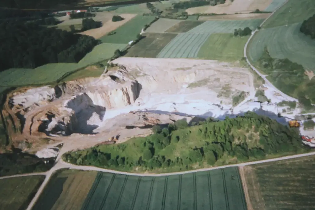 Bschor GmbH: Luftaufnahme eines großen offenen Steinbruchs, der von grünen Feldern und Straßen umgeben ist, mit freiliegender Erde und Maschinen im Abbaugebiet.