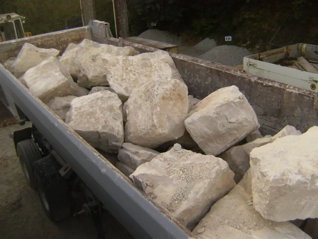 Bschor GmbH: Eine mit großen, unregelmäßig geformten Kalksteinbrocken gefüllte Kippmulde, die auf einer Baustelle oder in einem Steinbruch abgestellt ist.