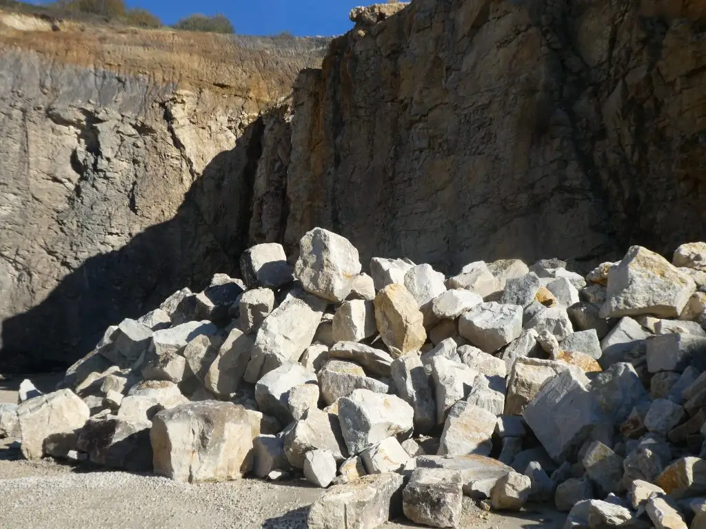Bschor GmbH: Ein Haufen Wasserbruchsteine liegt am Fuße einer hohen, zerklüfteten Klippe in einem felsigen Außenbereich.