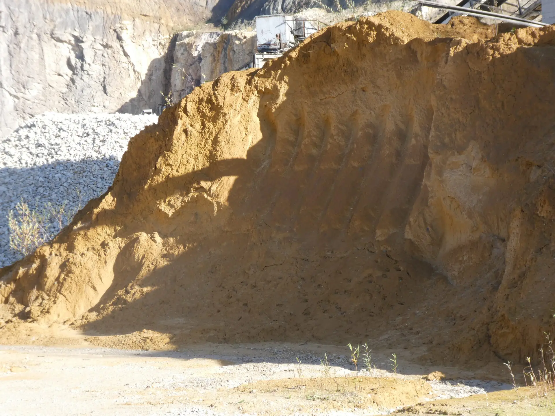 Bschor GmbH: Ein großer Sandhaufen mit sichtbaren Reifen- oder Reifenspuren liegt in einem Steinbruch, mit Steinschutt und Felswänden im Hintergrund.
