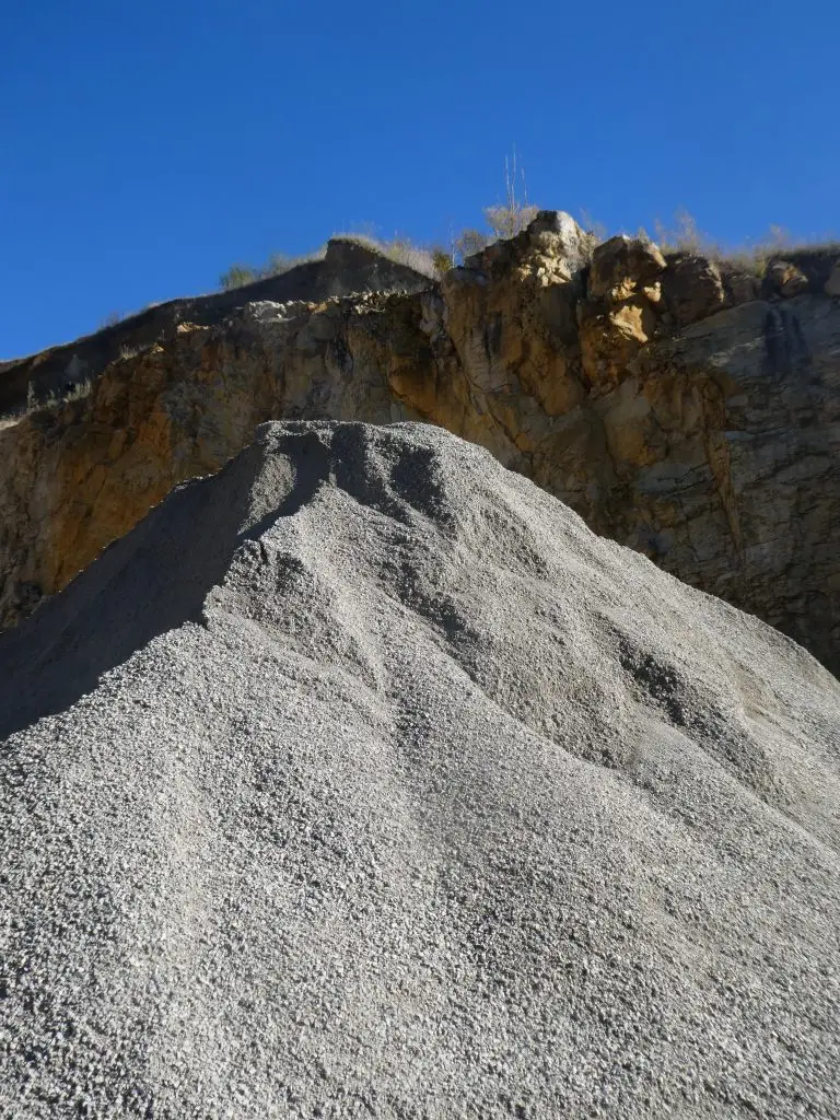 Bschor GmbH: Ein großer Kieshaufen liegt vor einer Felsklippe unter einem strahlend blauen Himmel.