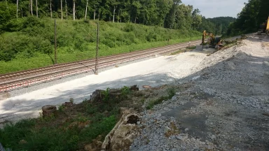 Bschor GmbH: Baustelle entlang eines Bahngleises mit Baggern und Schotter, angrenzend an ein Waldgebiet.